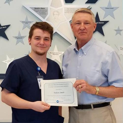 An older gentleman standing next to a young gentleman receiving his scholarship