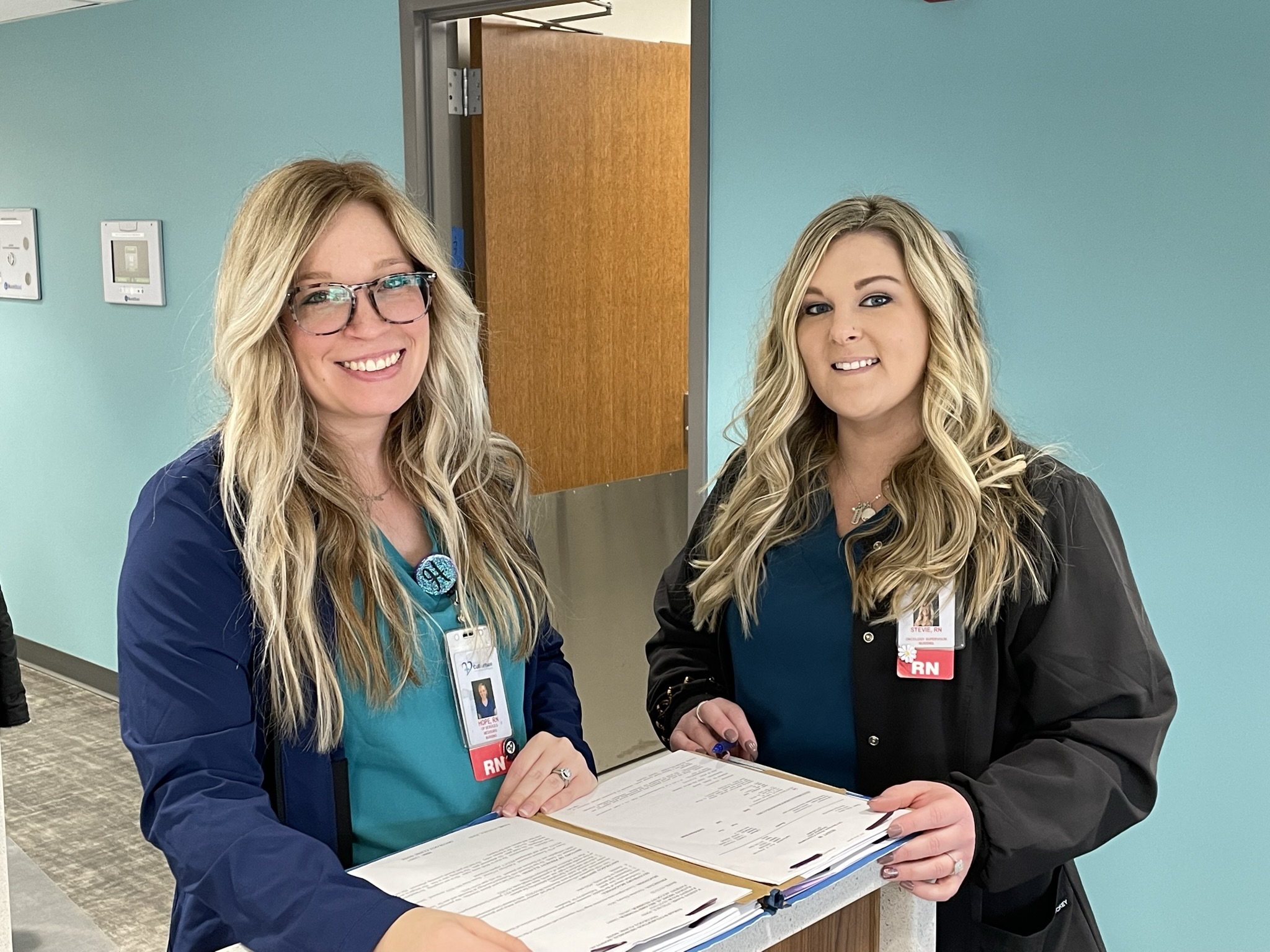 two infusion center nurses standing beside each other going over information from a paper